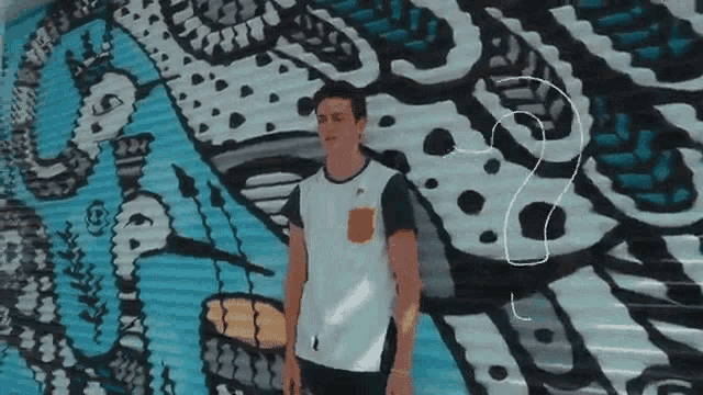 a young man stands in front of a mural that says ' a ' on it