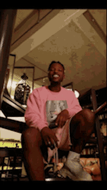 a man in a pink sweatshirt sits on a set of stairs with his legs crossed