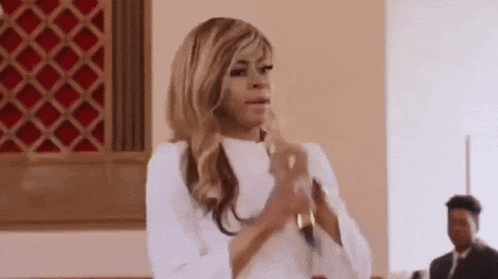 a woman in a white dress is clapping her hands in a church while holding a microphone .