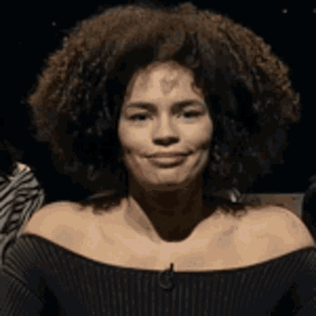 a woman with a large afro is smiling and wearing a black sweater .