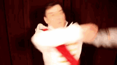 a man in a white shirt and red tie is standing in front of a red curtain with his arms outstretched .
