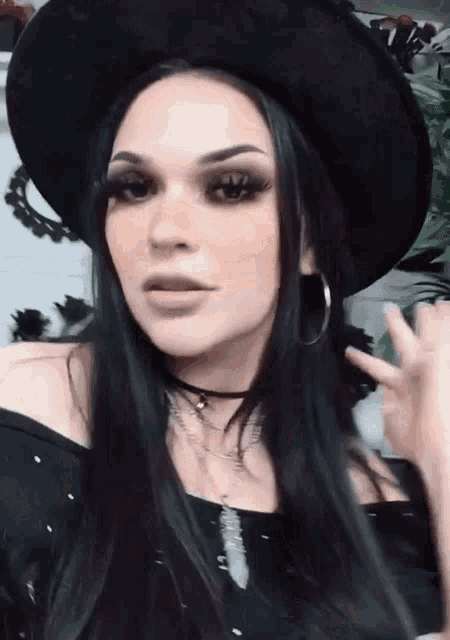 a woman with long black hair wearing a black hat and earrings .
