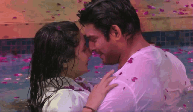a man and a woman are kissing in a pool surrounded by petals