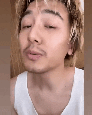 a man with a beard is wearing a white tank top and making a funny face .