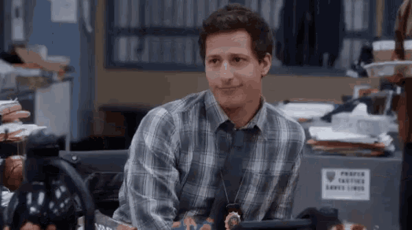 a man in a plaid shirt and tie is sitting at a desk in a police station .