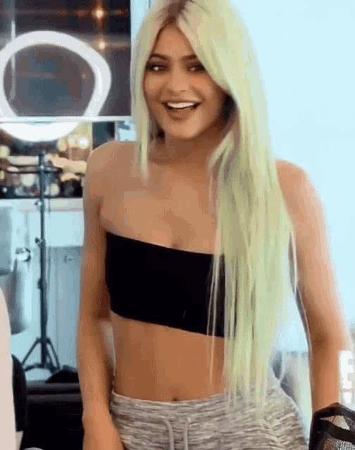 a woman with long green hair is wearing a black crop top and grey shorts .