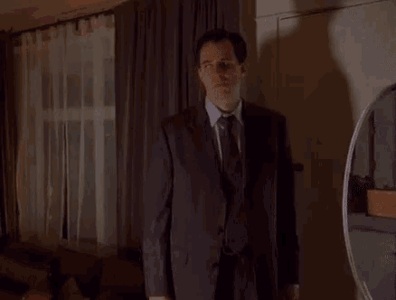 a man in a suit and tie is standing in a dark room in front of a mirror .