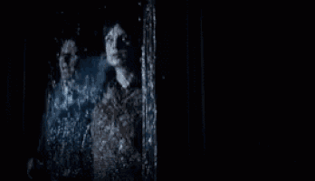 a man and a woman are looking out of a window while it rains .