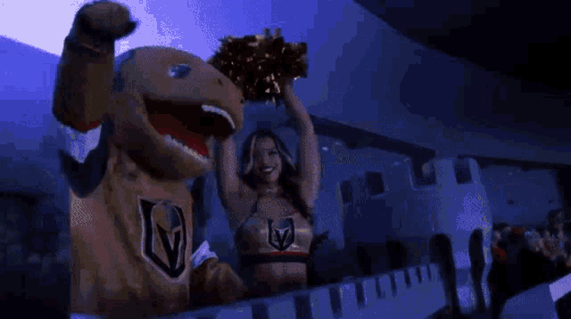 a cheerleader is holding up pom poms next to a mascot wearing a jersey with the letter v on it