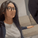 a woman wearing glasses is sitting on a couch looking at the camera .