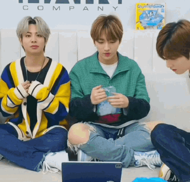 three young men are sitting on the floor in front of a company logo