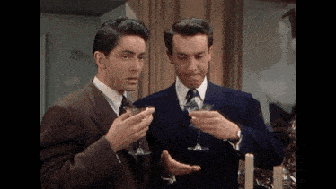 two men in suits and ties are toasting with wine glasses