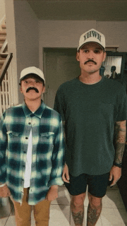 two men standing next to each other with one wearing a hat that says hawaii