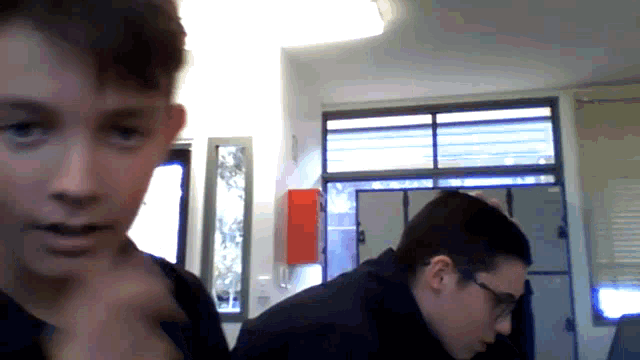 a boy with glasses looks at the camera while another boy looks on