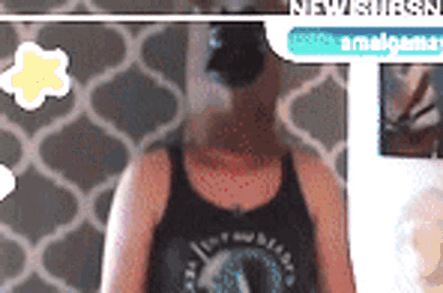 a woman wearing a black tank top is standing in front of a wall
