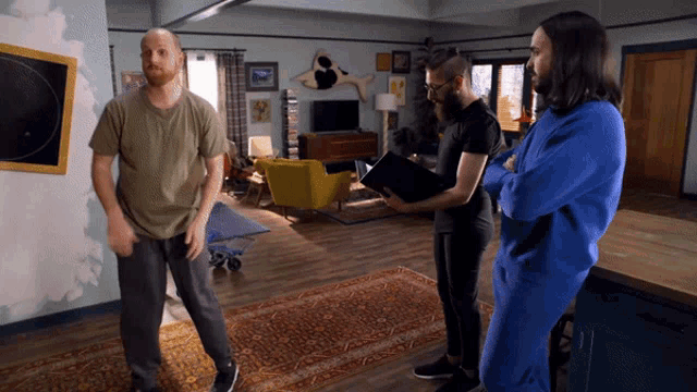 three men are standing in a living room with one holding a book