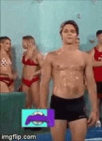 a man without a shirt is standing in a pool with women in bikinis behind him .