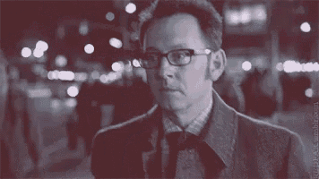 a man wearing glasses and a suit is standing in a crowded street at night .