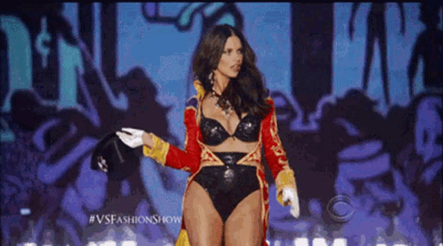 a woman in a bra and gloves is walking down a runway at a fashion show