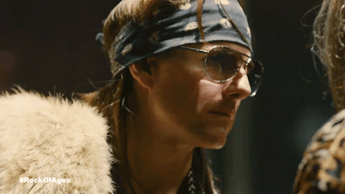 a close up of a person wearing glasses and a headband with the hashtag #rockofages