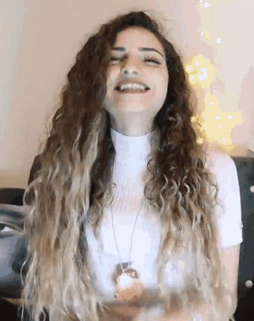 a woman with long curly hair wearing a white turtleneck and a necklace