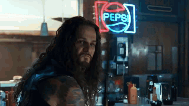 a man with long hair is standing in front of a pepsi neon sign .