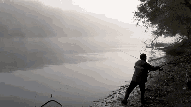 a man is fishing on the shore of a foggy river .