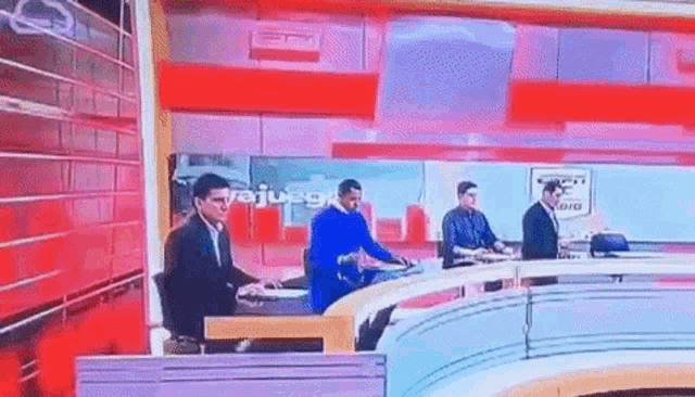 a group of men are sitting at a table in front of a large screen that says ' juego ' on it