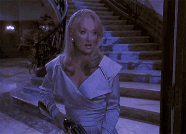 a woman in a white dress is standing in front of a set of stairs holding a gun .