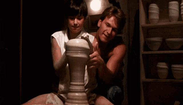 a man and a woman are sitting next to each other looking at a pottery wheel