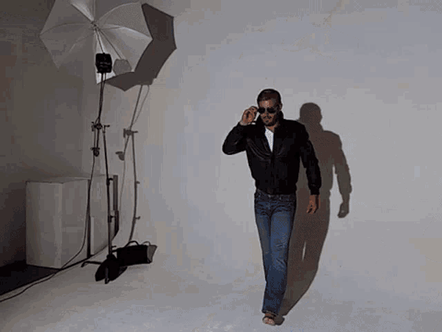 a man wearing sunglasses and a leather jacket walks in front of a white umbrella