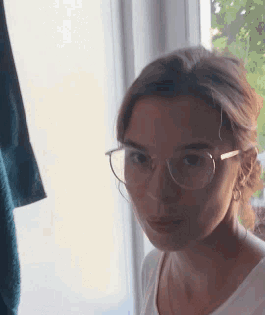 a woman wearing glasses and hoop earrings looks at the camera