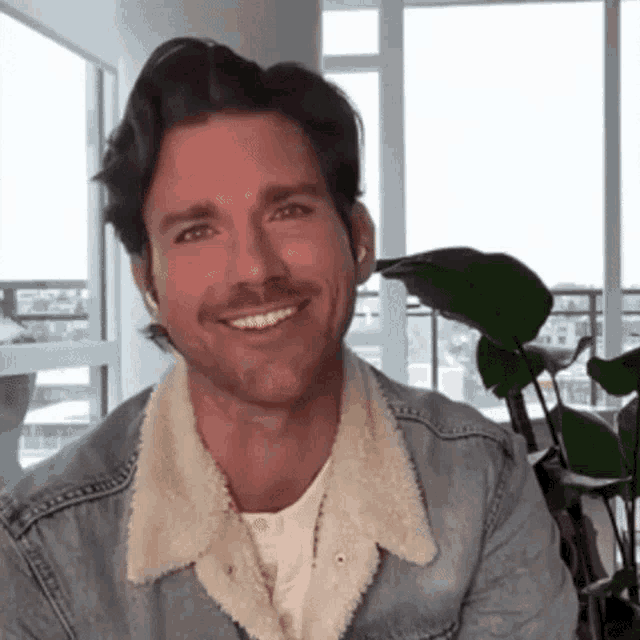 a man is wearing a denim jacket with a fur collar and smiling .