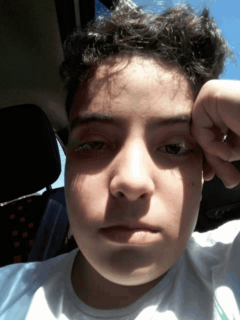 a young boy with curly hair holds his hand to his forehead