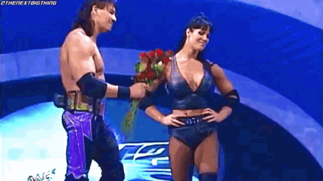 a wrestler is giving a bouquet of flowers to a woman on a stage .