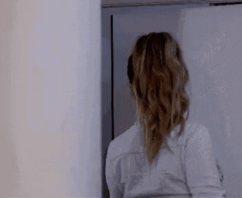 a woman in a white shirt is standing in front of a door and looking at herself in the mirror .