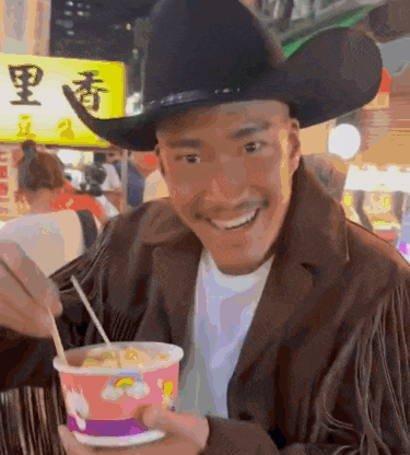 a man wearing a cowboy hat is smiling while holding a cup of food