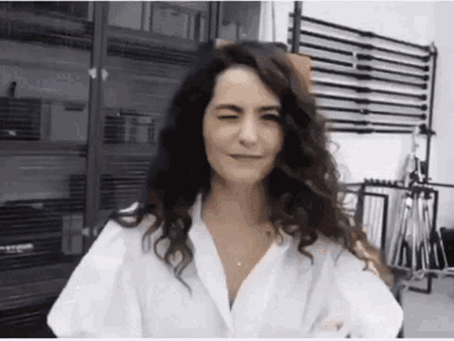 a woman with curly hair is wearing a white shirt and smiling with her eyes closed .