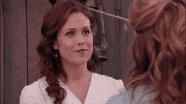two women are standing next to each other and looking at each other . one of the women has red hair and the other has blue hair .