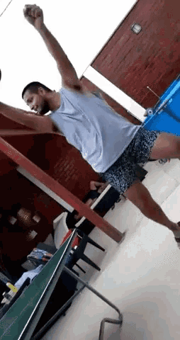 a man in a white tank top and shorts is jumping in the air while playing ping pong