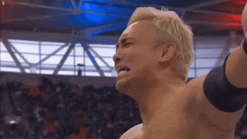 a man with blonde hair is wrestling in a stadium with his arms in the air .