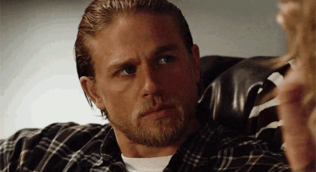 a man with a beard wearing a plaid shirt is looking at something