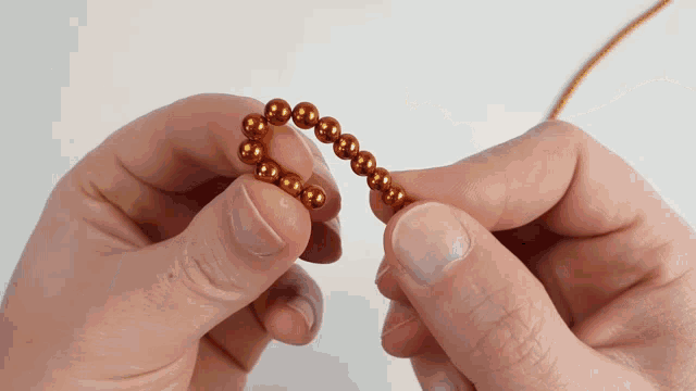 a person is holding a string of copper beads