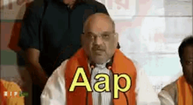 a man wearing an orange scarf is giving a speech in front of a microphone and says aap .