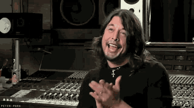 a man with long hair and a beard is sitting in front of a mixer in a recording studio .