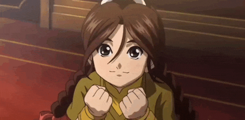 a little girl with brown hair is sitting on the floor with her hands in her fist .