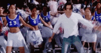 a man is dancing in front of a crowd of cheerleaders wearing blue and white uniforms .