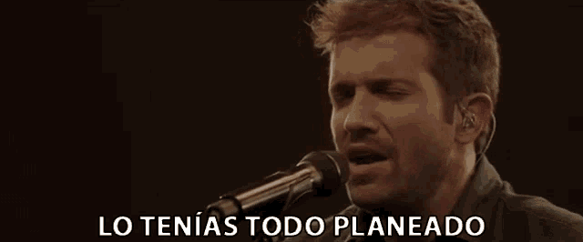 a man singing into a microphone with the words " lo tenias todo planeado " below him