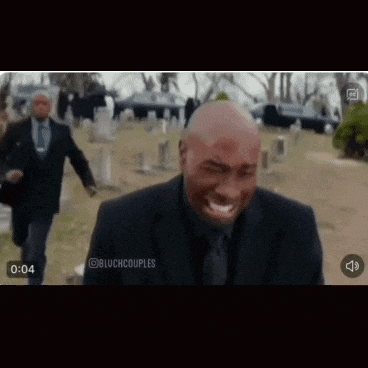 a man in a suit and tie is crying in a cemetery while another man runs behind him .