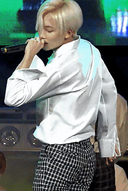 a man in a white shirt and plaid pants singing into a microphone